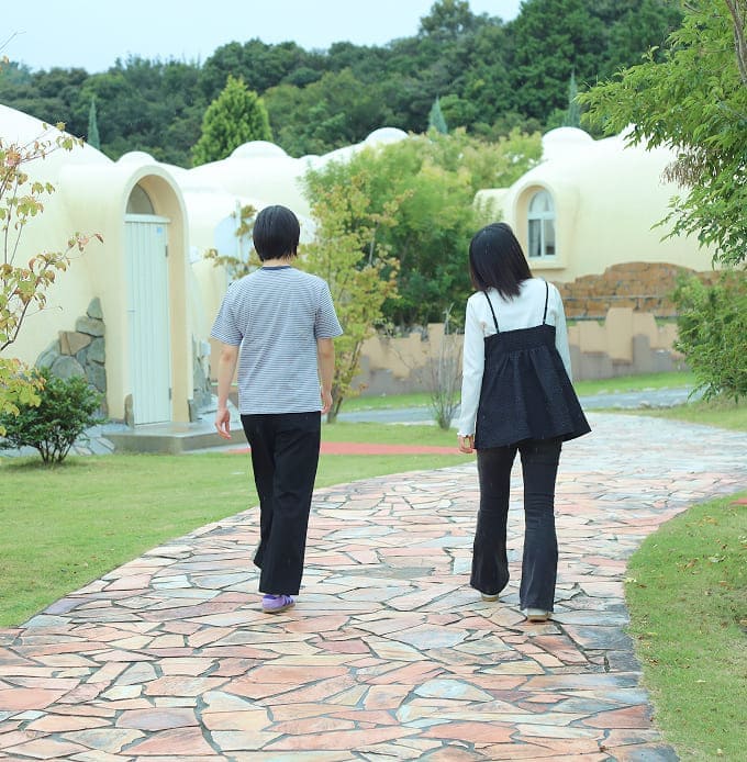 石畳の小道を2人が並んで歩いている、背景にドーム型の建物がある