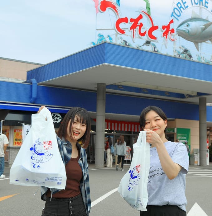 店の前で2人が買い物袋を持ってポーズをとっている