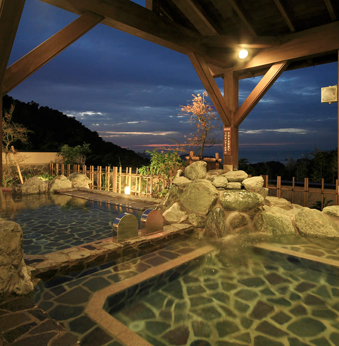 夜景を望む屋根付き露天風呂、岩や植栽に囲まれている
